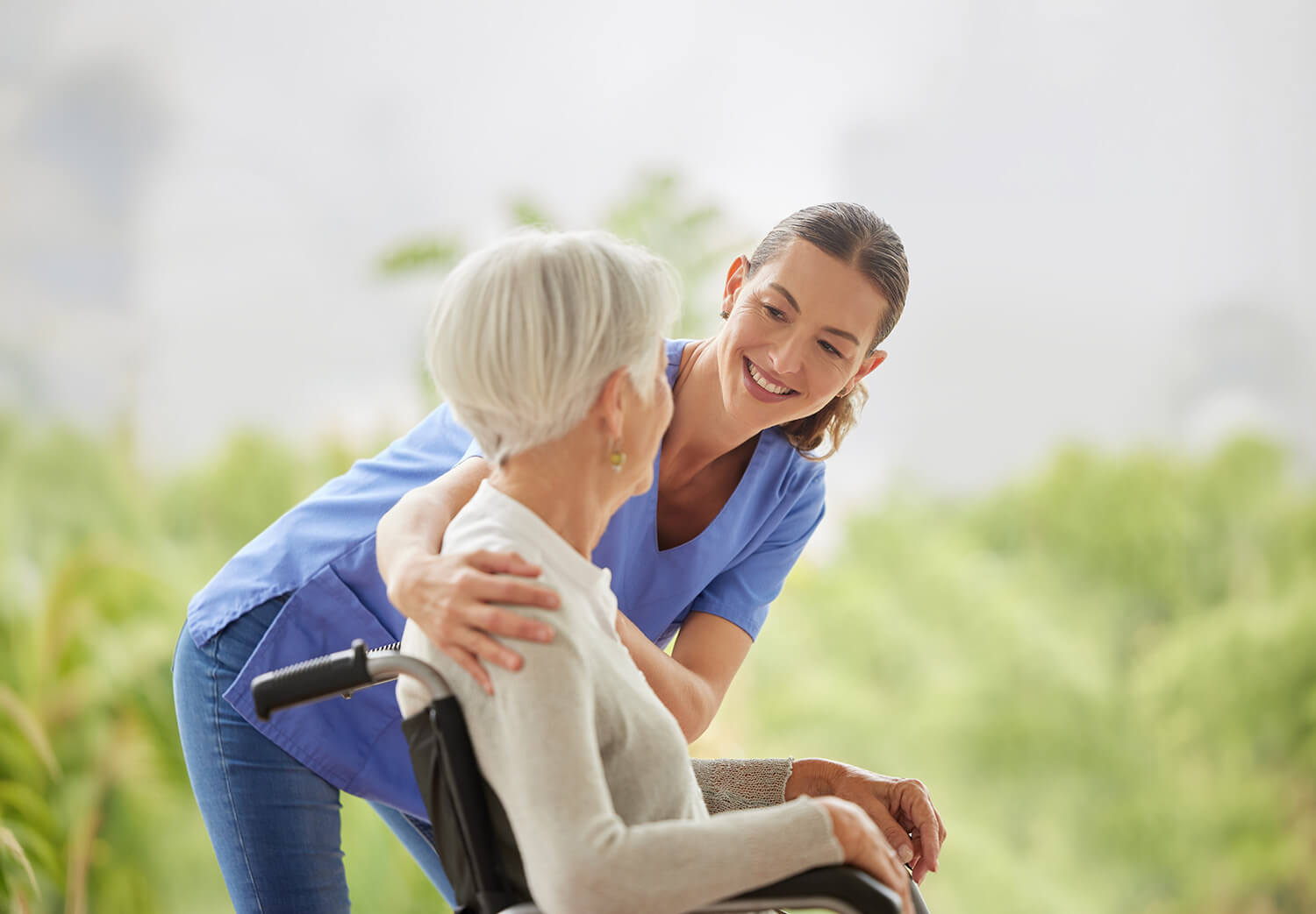 Betreuungskraft begleitet eine Seniorin im Rollstuhl draußen