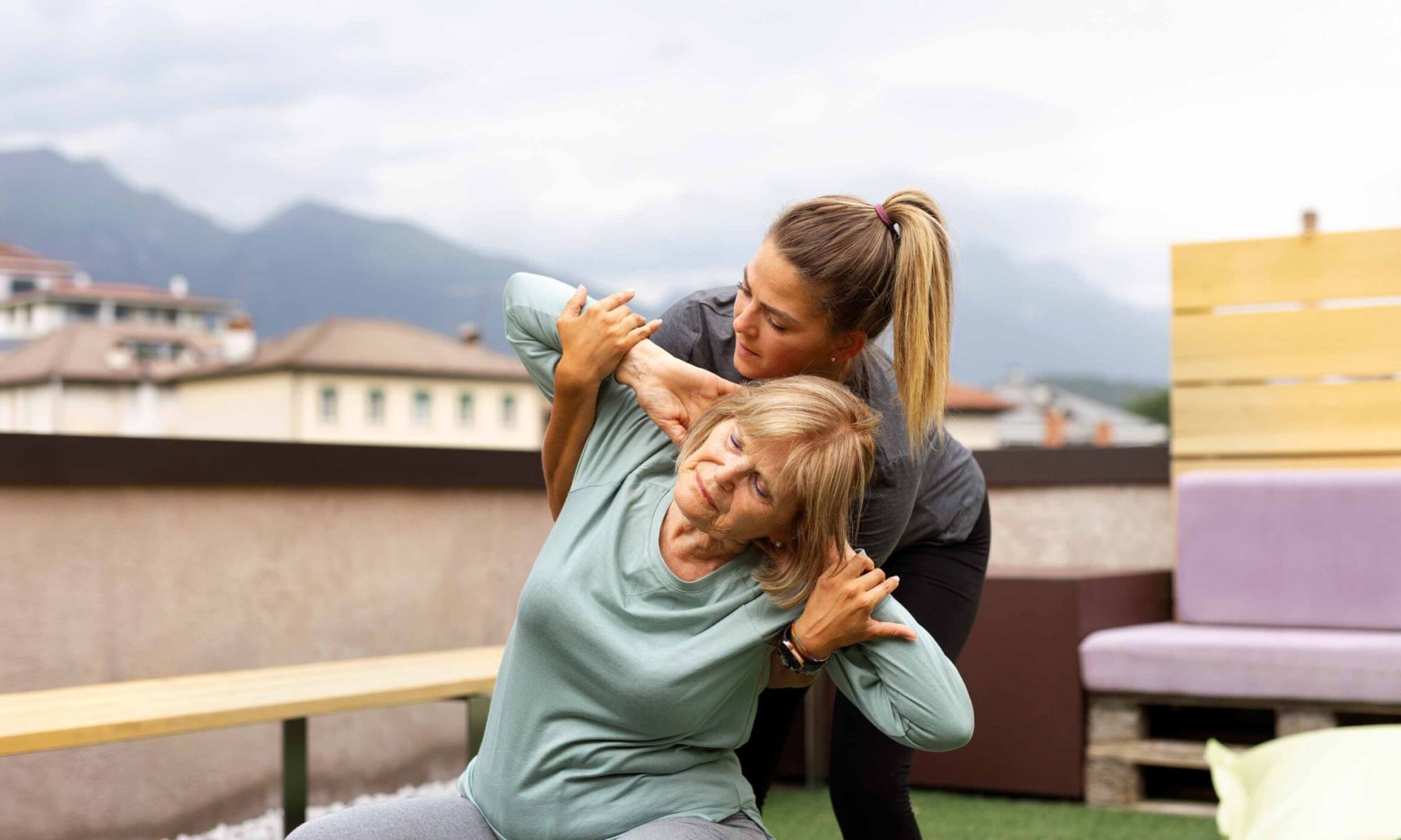 Betreuungskraft umarmt eine ältere Frau auf einer Terrasse