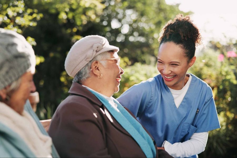 Pflegekraft spricht mit zwei Seniorinnen im Garten
